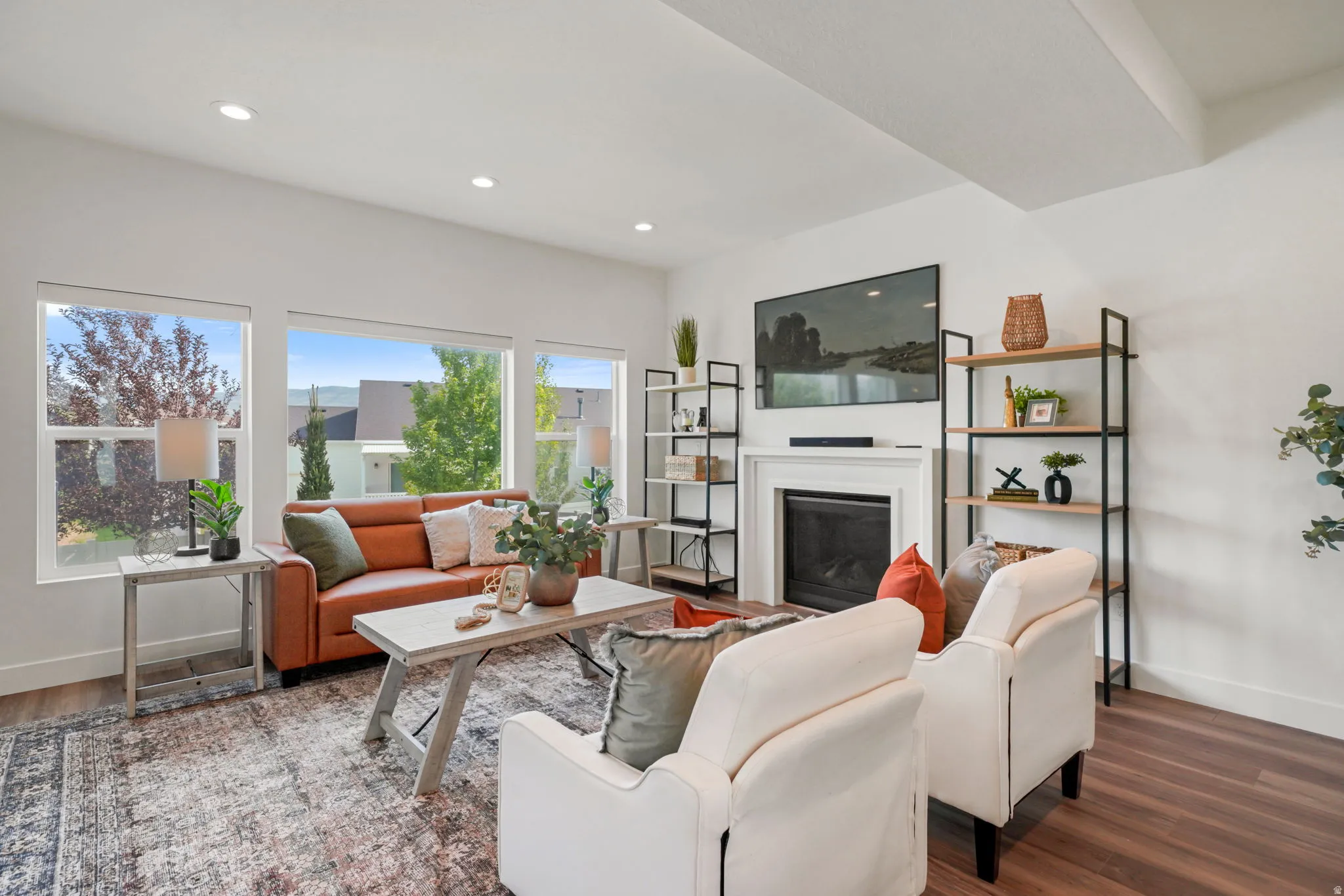 Bright, open living room showcasing soaring ceilings with recessed lighting, large multi-pane windows flooding the space with natural light, and hardwood flooring throughout