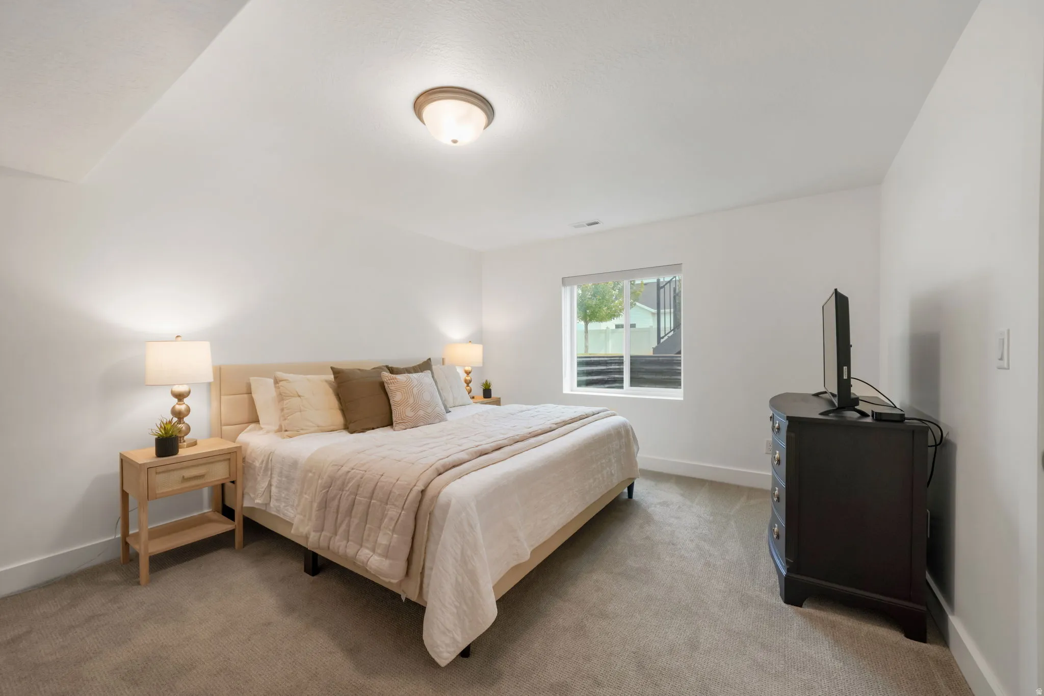 Bright primary bedroom with vaulted ceilings, recessed lighting, and a large bed frame