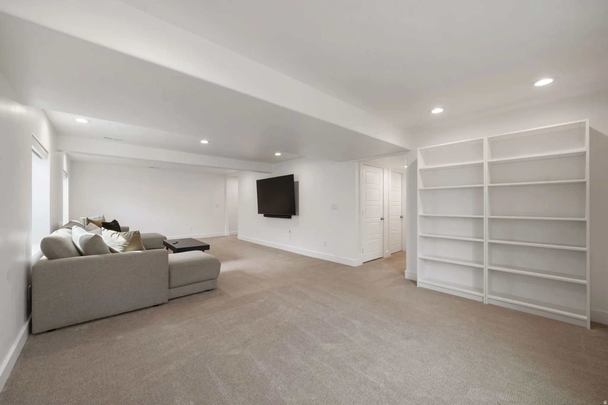 Spacious recreation room featuring neutral wood-finish flooring, recessed ceiling lighting, and a wall-mounted flat-screen display