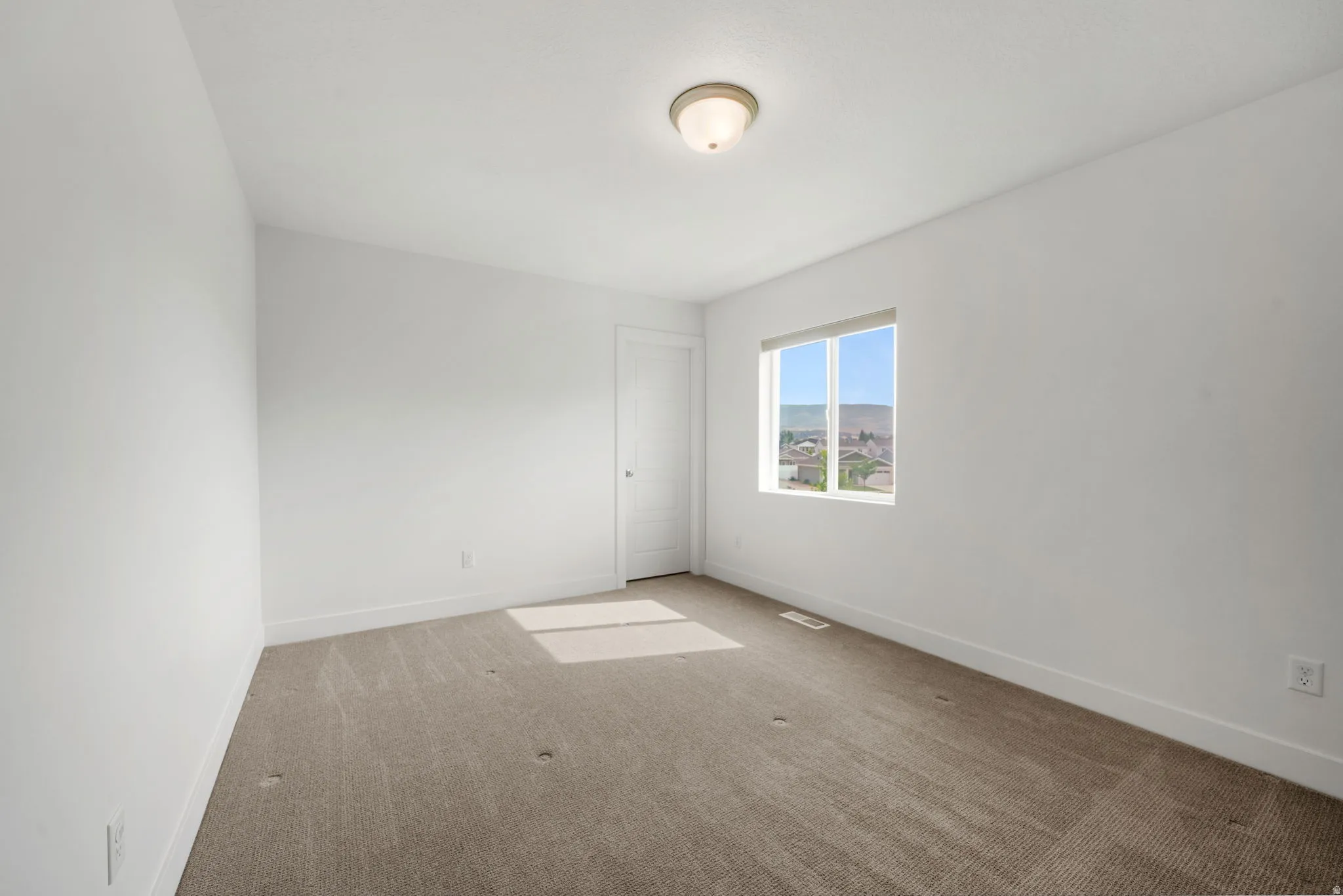 Spacious interior featuring carpeted flooring, white walls, a single window, and a flush mount light fixture