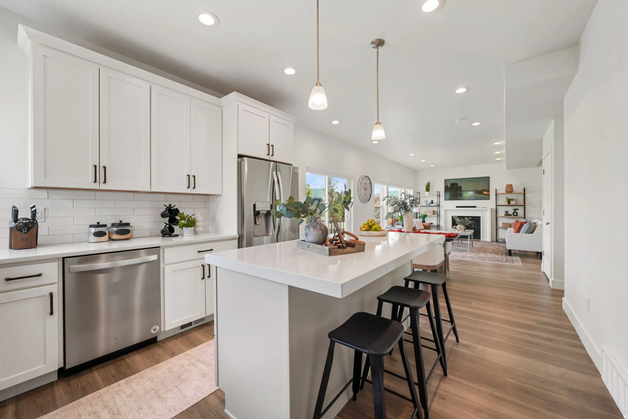 Modern kitchen and dining area featuring white cabinetry with brushed nickel hardware, stainless steel appliances including a dishwasher and gas cooktop, quartz waterfall island countertop, pendant lighting, recessed ceiling lights, wide-plank wood-finish