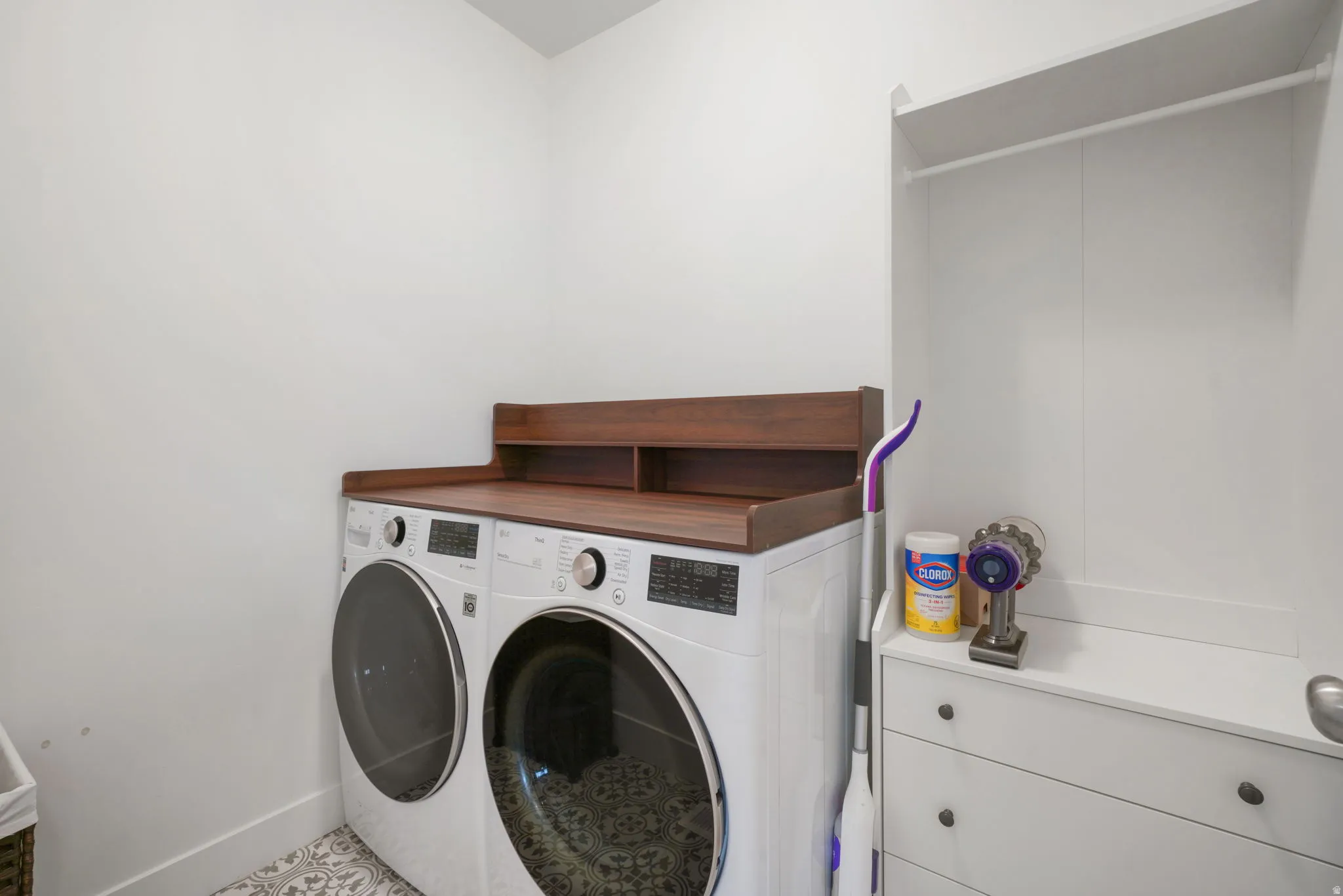 Dedicated laundry room featuring side-by-side front-load washers and dryers with wood-finish countertop workspace, white cabinetry with drawer storage, and terrazzo-style flooring