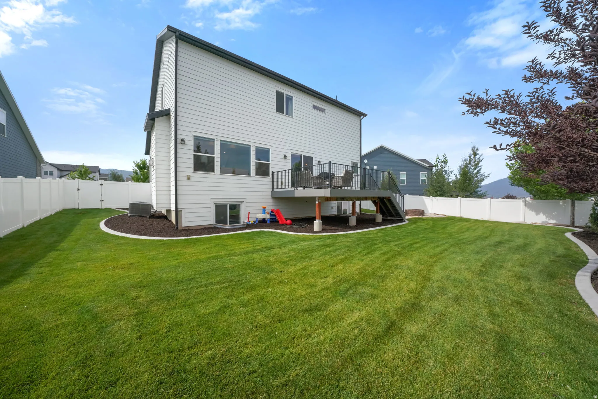 Expansive backyard featuring a manicured lawn, white vinyl fencing, a raised deck with dark railing, and a walk-out basement