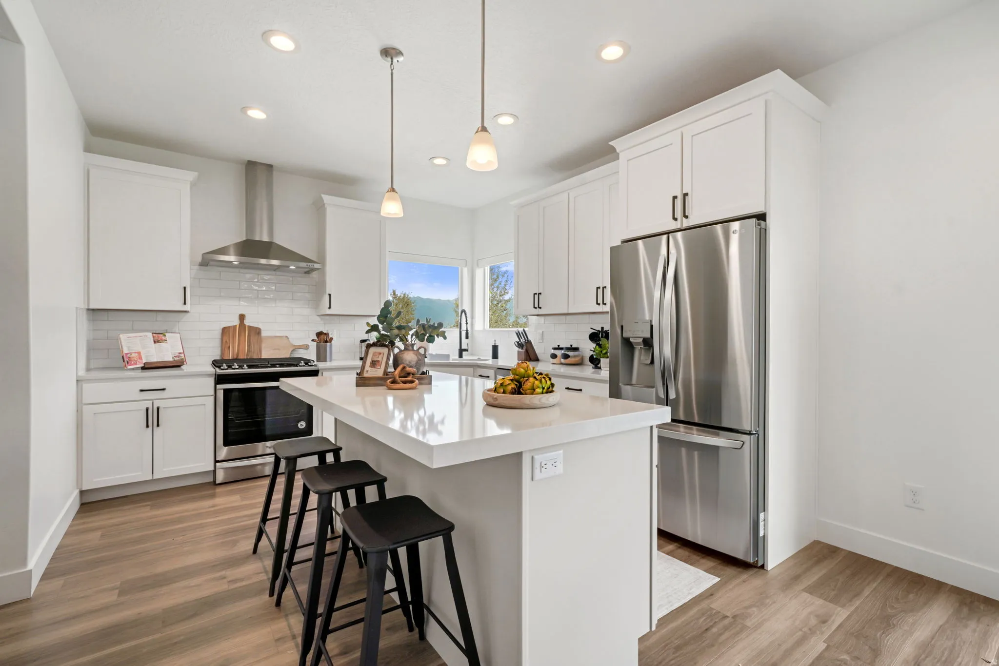 Kitchen featuring white shaker cabinetry, stainless steel appliances, wood-finish flooring, a center island with pendant lighting, and a subway tile backsplash