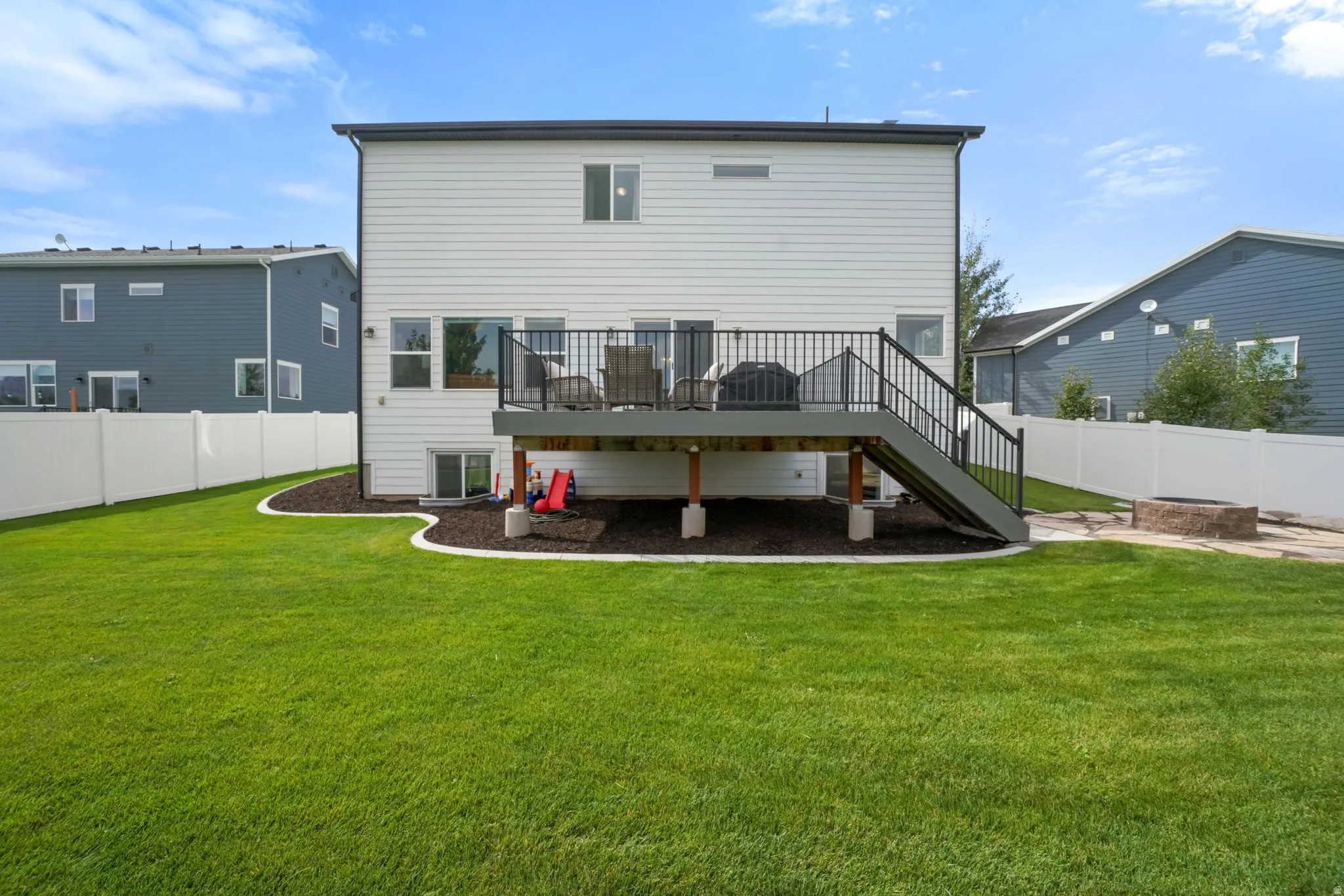 Expansive lawn with a white privacy fence, multi-level deck with black railings, and a stone fire pit