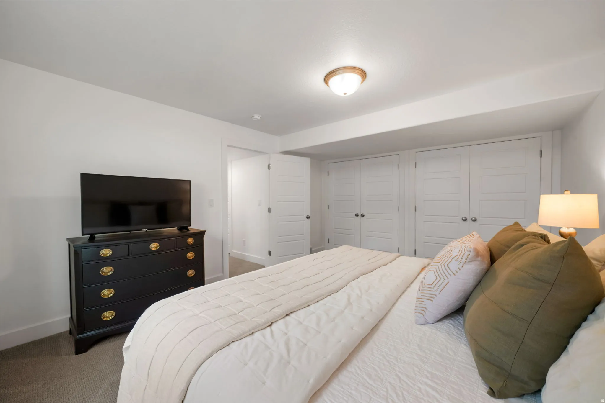 Spacious primary bedroom featuring neutral carpeting, recessed ceiling lighting, and a black dresser with brass hardware