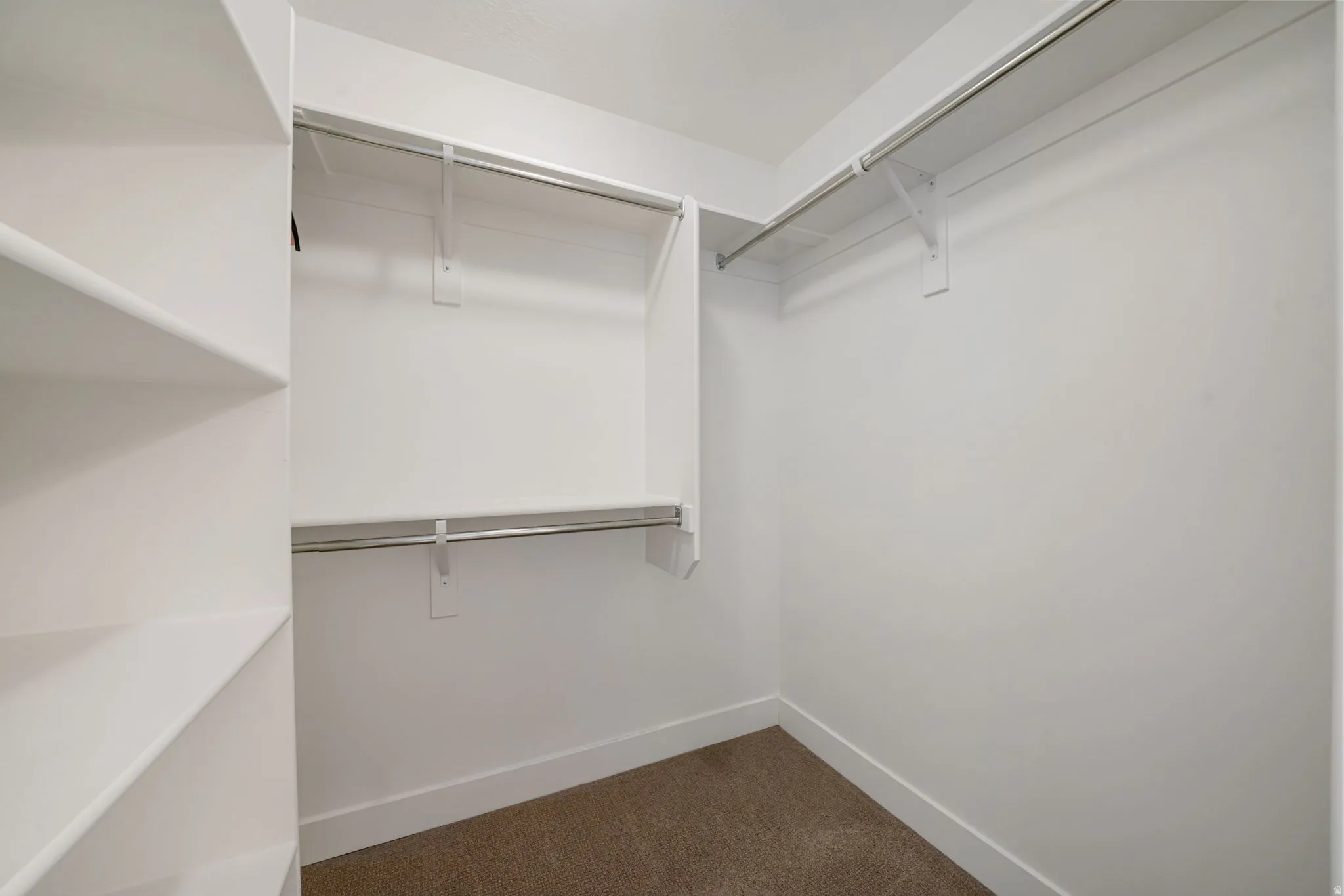 Built-in shelving, multiple hanging rods, white walls, and carpet flooring