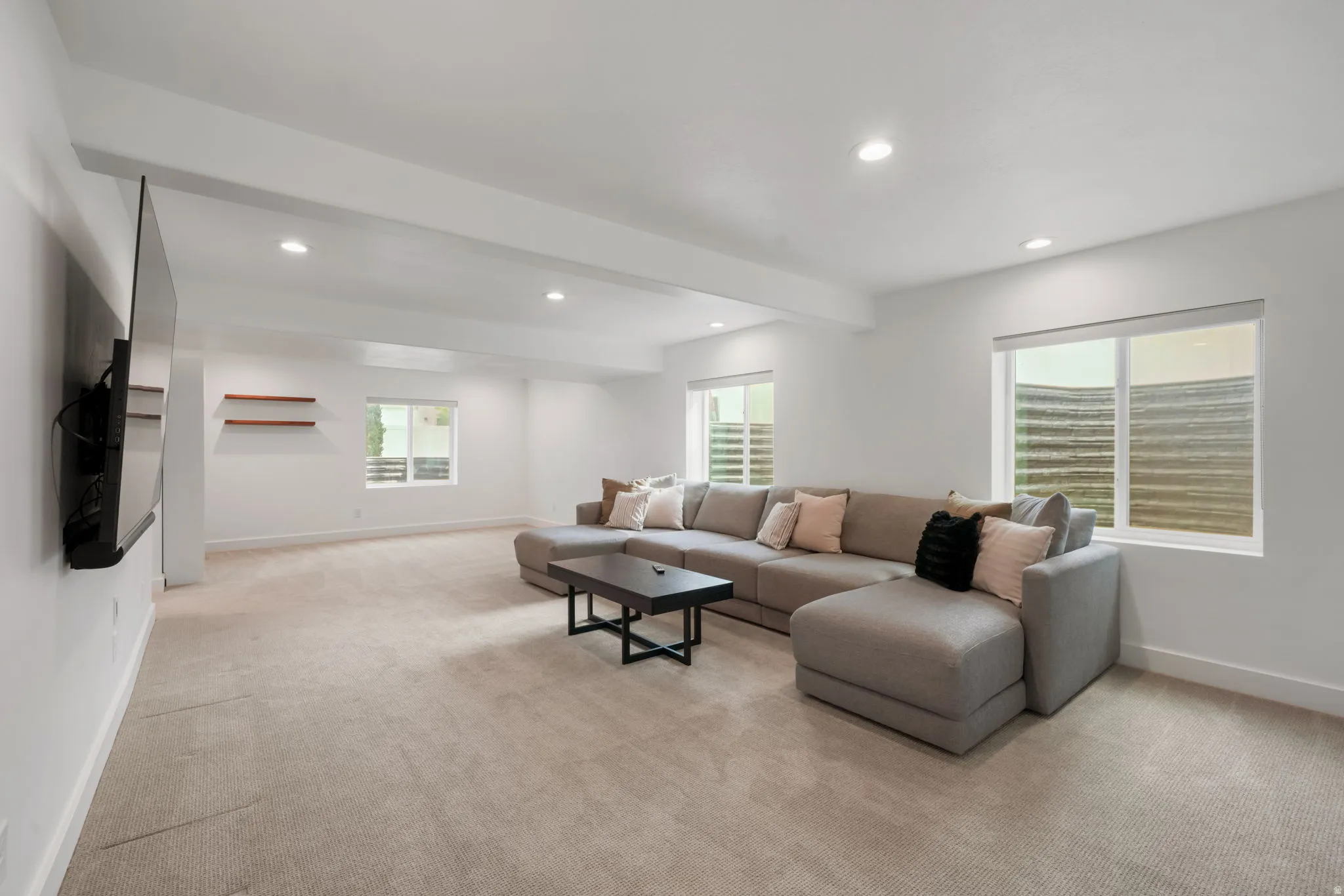 Spacious recreational room featuring neutral wood-finish flooring throughout, recessed ceiling lighting, and large windows with plantation shutters providing natural light