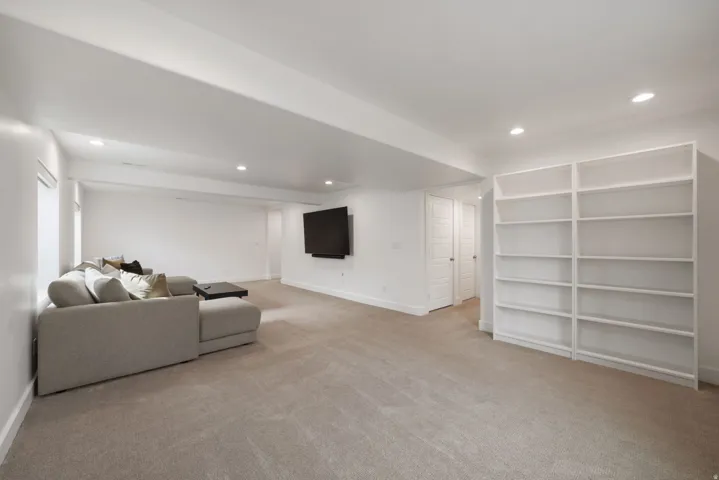 Spacious recreation room featuring neutral wood-finish flooring, recessed ceiling lighting, and a wall-mounted flat-screen display