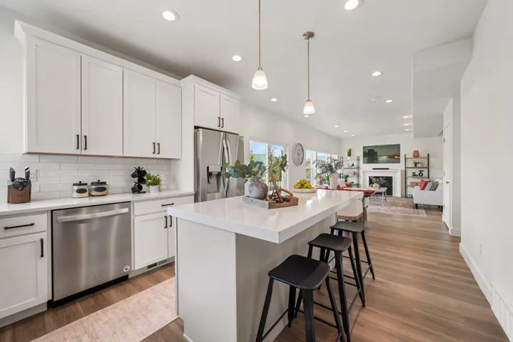 Modern kitchen and dining area featuring white cabinetry with brushed nickel hardware, stainless steel appliances including a dishwasher and gas cooktop, quartz waterfall island countertop, pendant lighting, recessed ceiling lights, wide-plank wood-finish
