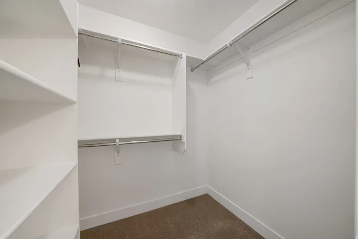 Built-in shelving, multiple hanging rods, white walls, and carpet flooring