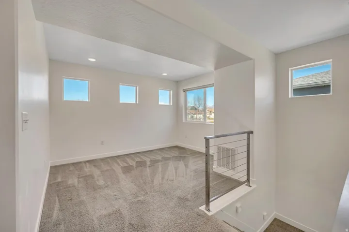 Open upper-level space featuring recessed lighting, multiple windows, and a stainless steel railing
