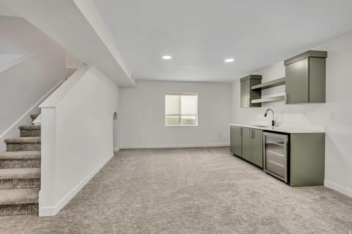 Built-in wet bar with green cabinetry, white countertop, and stainless steel sink