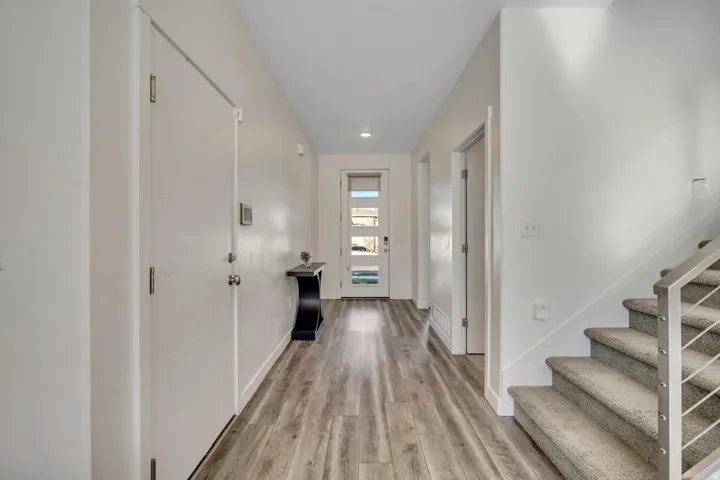 Bright entryway featuring wood-finish flooring, a modern front door with frosted glass panels, and a carpeted staircase with a metal railing