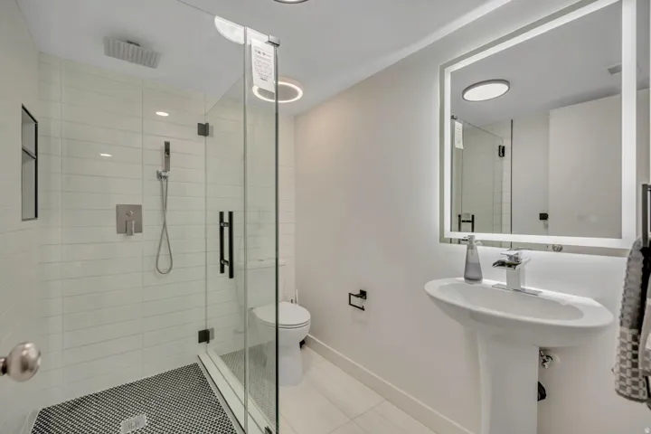 Glass-enclosed shower with a rainfall showerhead, white subway tile surround, and black penny tile flooring