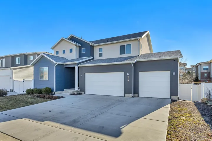 Contemporary exterior with gray stucco and blue siding, featuring two attached garages, a covered entry, and a concrete driveway