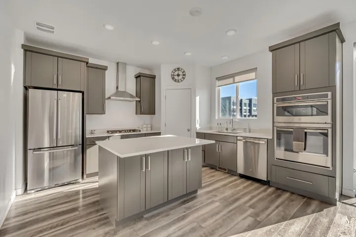 Modern kitchen featuring wood-finish flooring, recessed lighting, stainless steel appliances, a center island with a light-toned countertop, and grey cabinetry