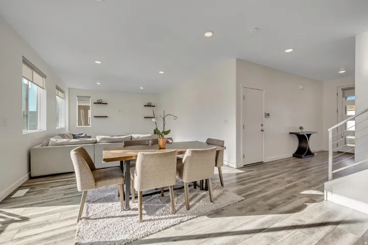Open-concept living space featuring wood-finish flooring, recessed lighting, multiple windows, and a modern staircase with horizontal railings