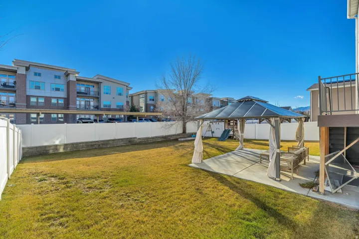 Expansive lawn area with a white privacy fence and a concrete patio featuring a gazebo