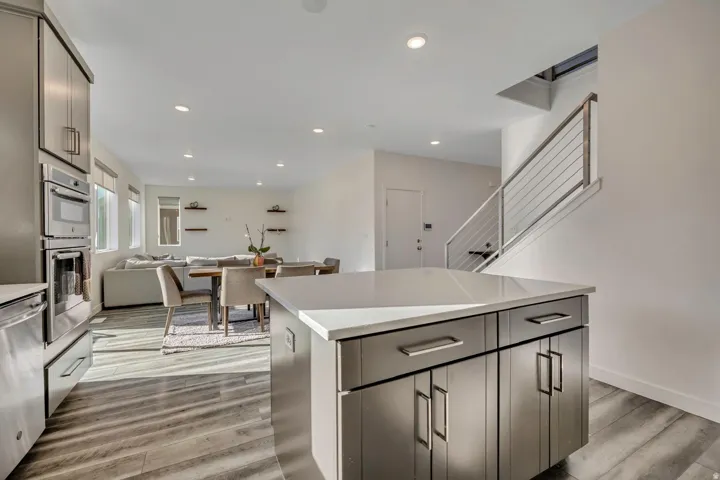 Kitchen island with stone countertop, stainless steel appliances, wood-finish flooring, recessed lighting, and a contemporary staircase with cable railing