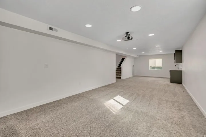 Spacious carpeted room featuring recessed lighting, built-in projector, and a wet bar with dark cabinetry and a stainless steel sink