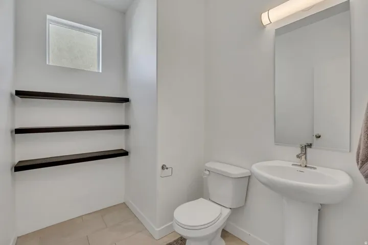 Pedestal sink with chrome faucet, wall-mounted mirror, overhead vanity lighting, and three dark wood-finish floating shelves