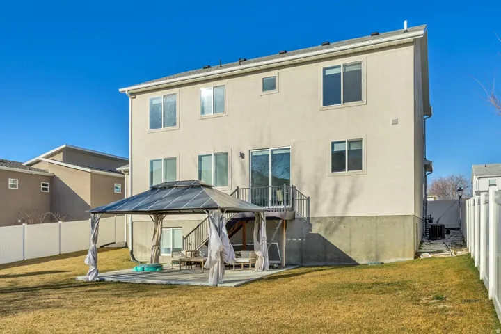 Cream stucco exterior with multiple windows, a second-story deck, and a ground-level patio featuring a gazebo