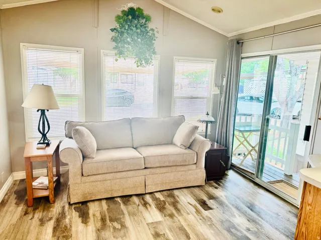 Vaulted ceiling, wood-finish flooring, multiple windows with blinds, sliding glass door, and exterior decking