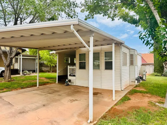 Attached carport with a concrete driveway, white siding exterior, and mature trees on the property