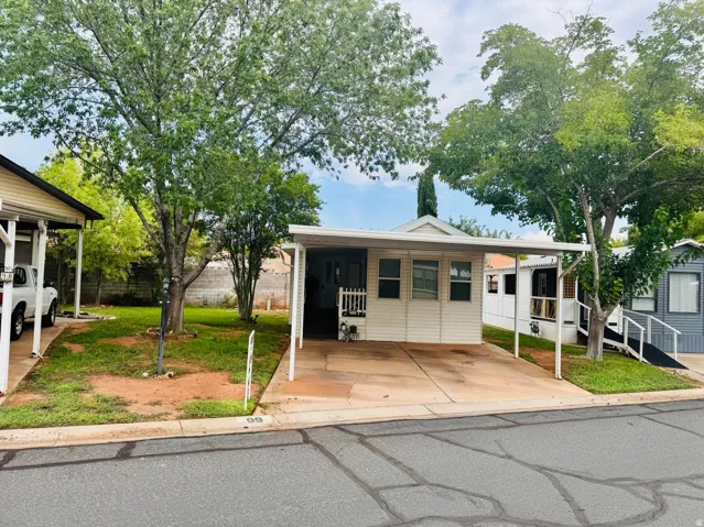 White horizontal siding exterior with a covered carport, mature trees, and a concrete driveway