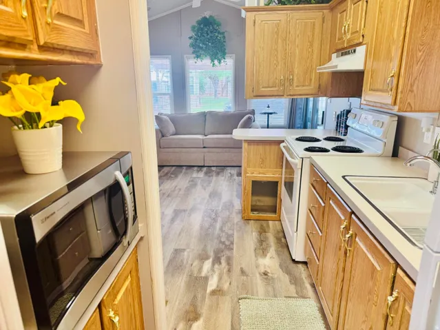 Wood-finish flooring throughout, kitchen with wood cabinetry, and white appliances