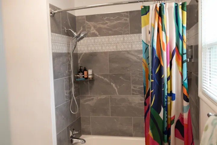 Bathtub with a tiled surround featuring large format grey tiles and a decorative accent band