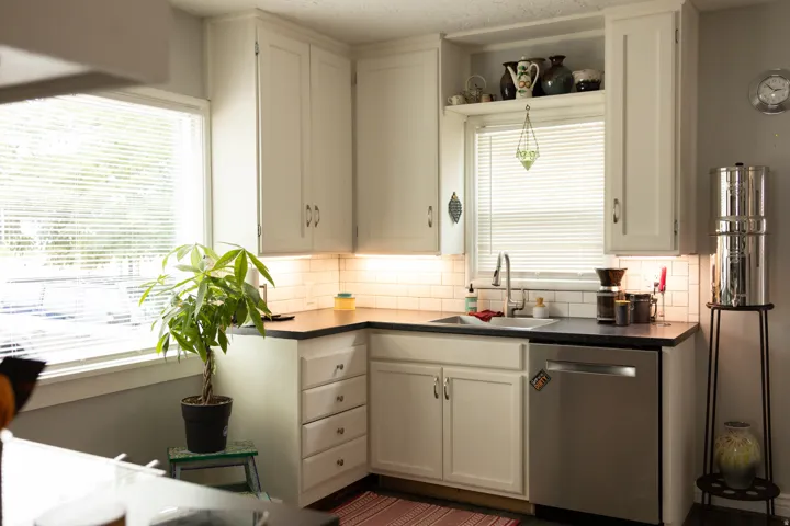 Crisp white cabinetry, corner windows, stainless steel dishwasher, undermount sink, and subway tile backsplash