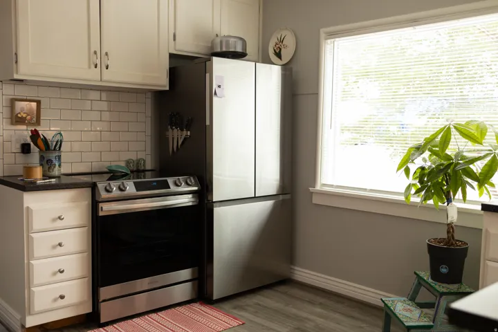 White shaker-style cabinetry with dark hardware, subway tile backsplash, dark countertop, stainless steel appliances, and wood-finish flooring