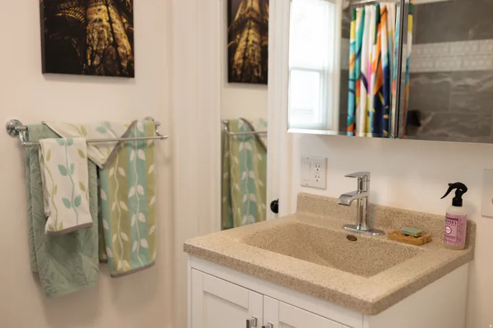 Vanity with integrated sink and chrome faucet, white paneled cabinetry, mirrored medicine cabinet, and tiled shower surround