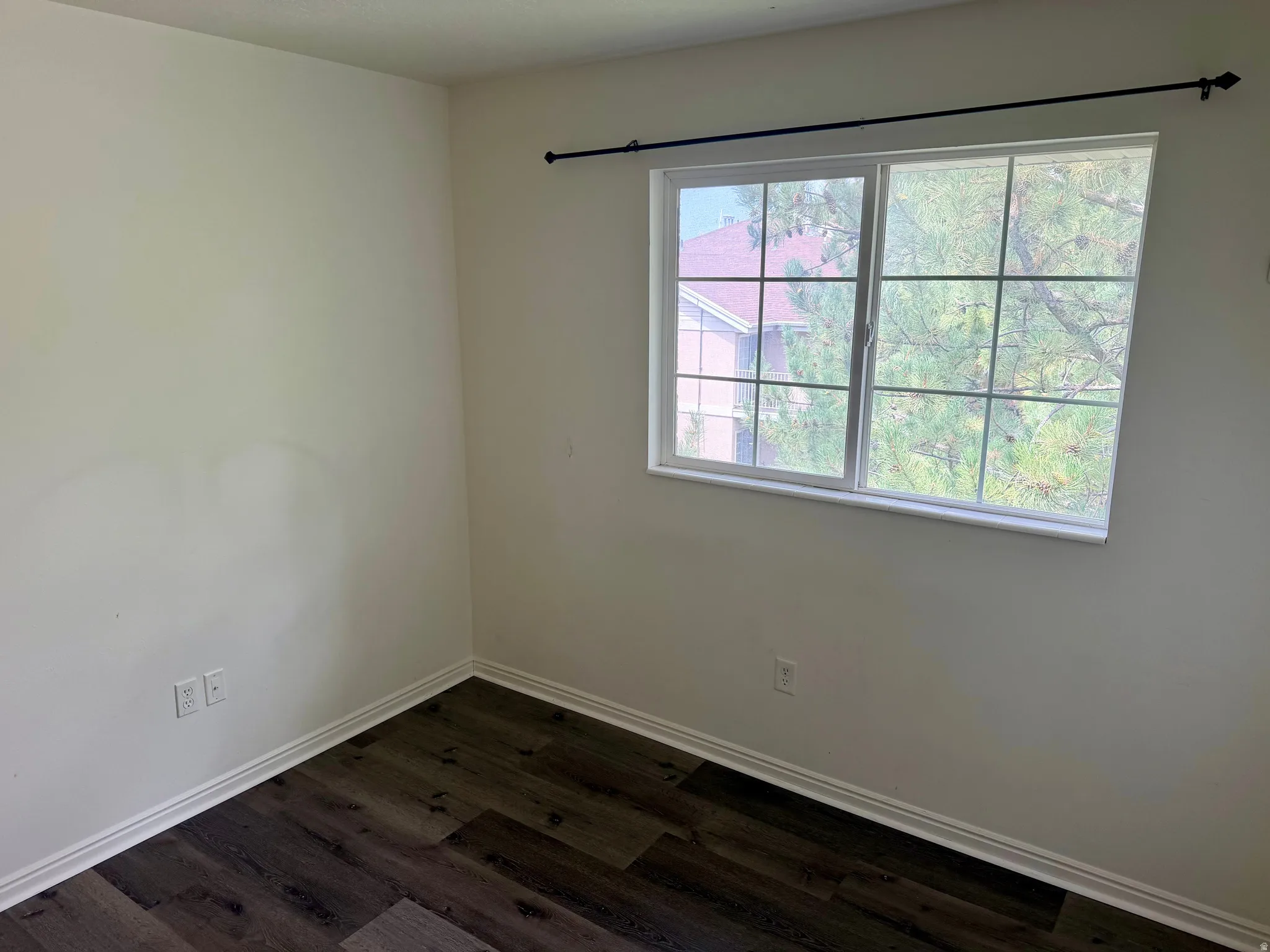 White walls with dark wood-finish flooring, featuring a window with white framing and grid panes