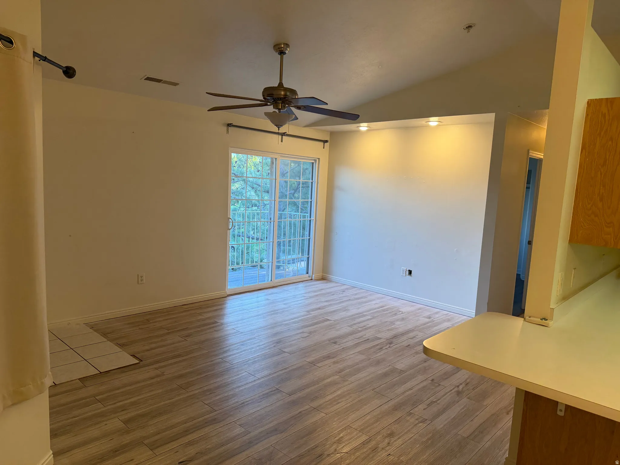 Vaulted ceiling with an attached ceiling fan, wood-finish flooring, sliding glass doors, built-in shelving with recessed lighting, and a kitchen pass-through