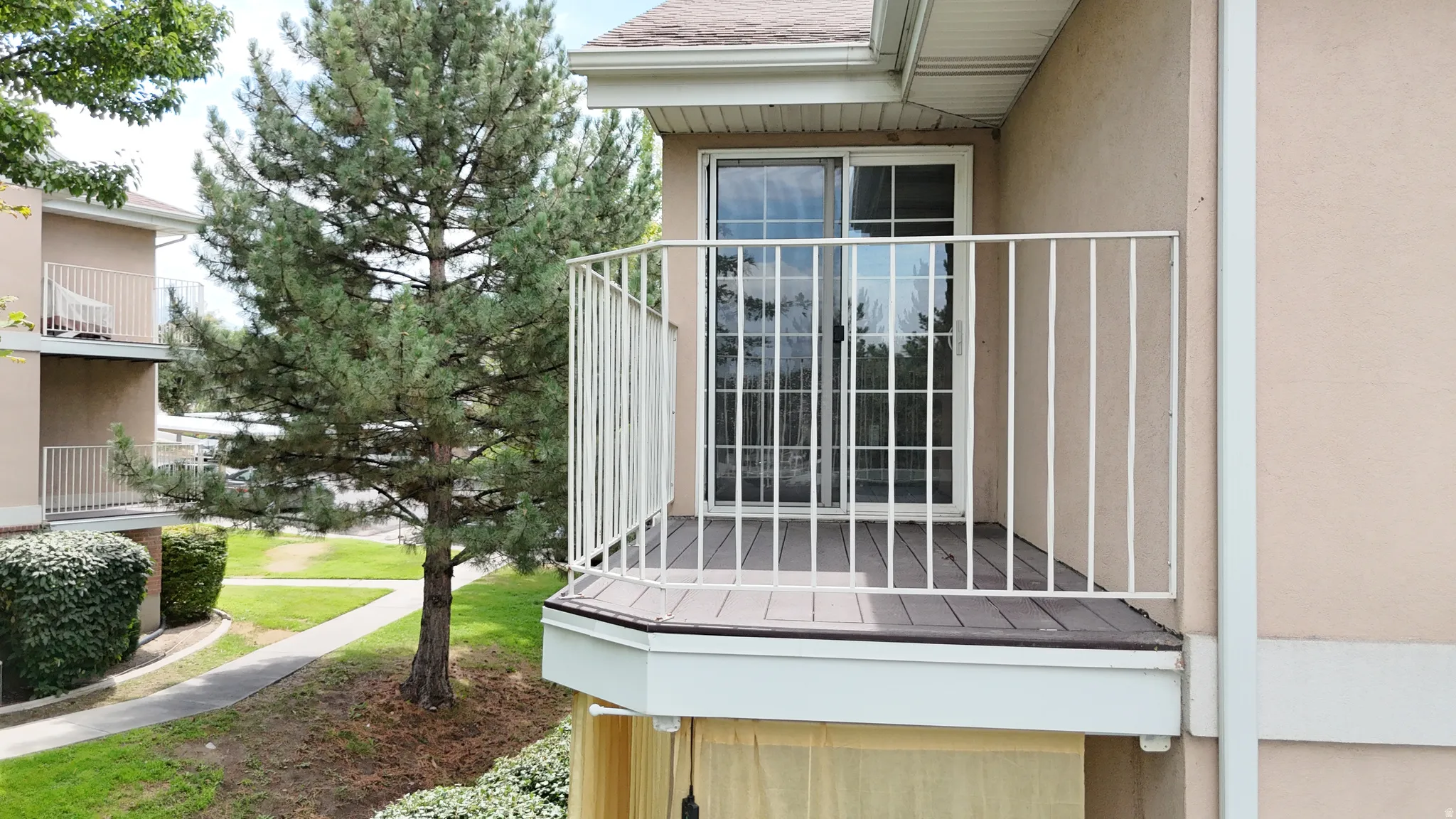 Private balcony with dark wood-finish flooring and white metal railing, featuring a sliding glass door