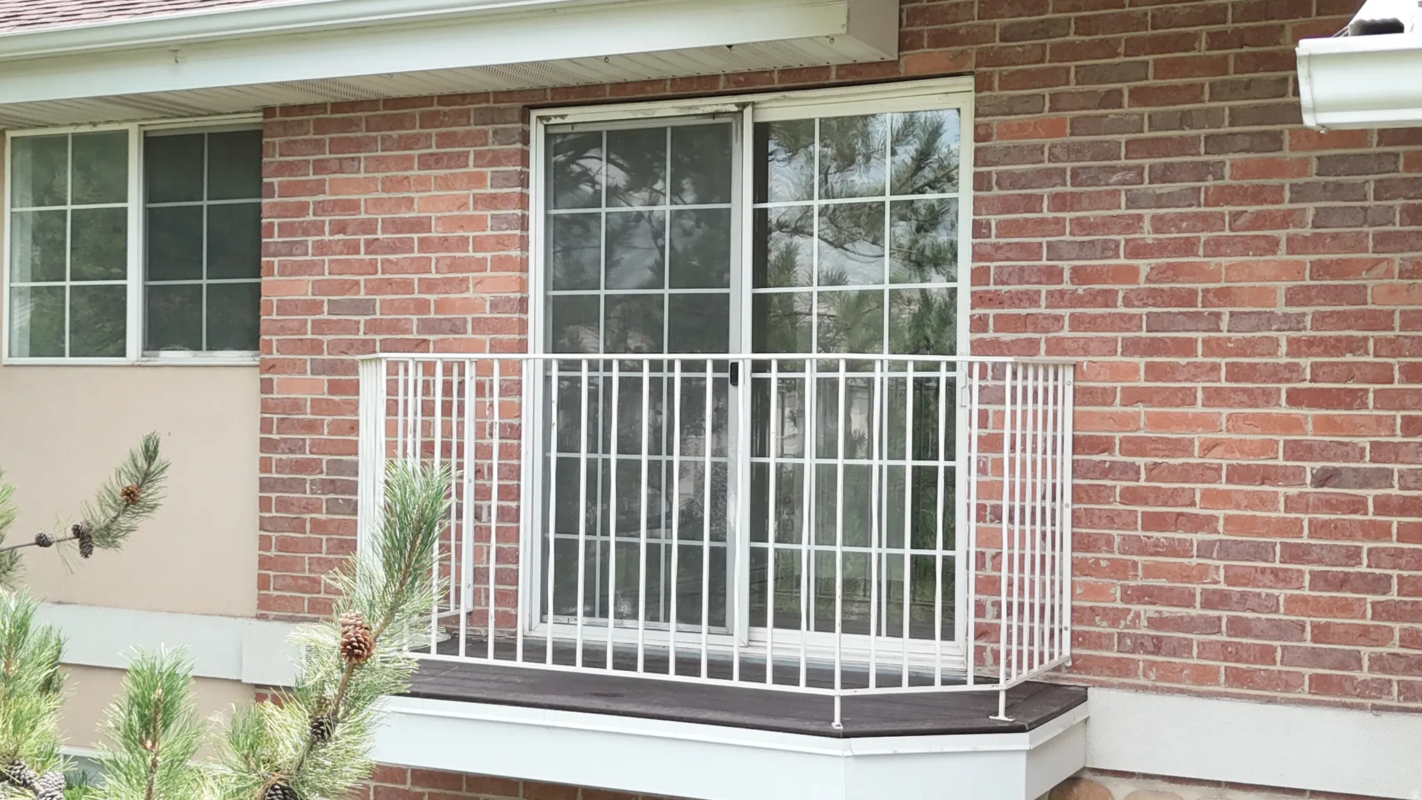 Brick exterior featuring a sliding glass door with grid panes, white railing, and exterior window with grid panes