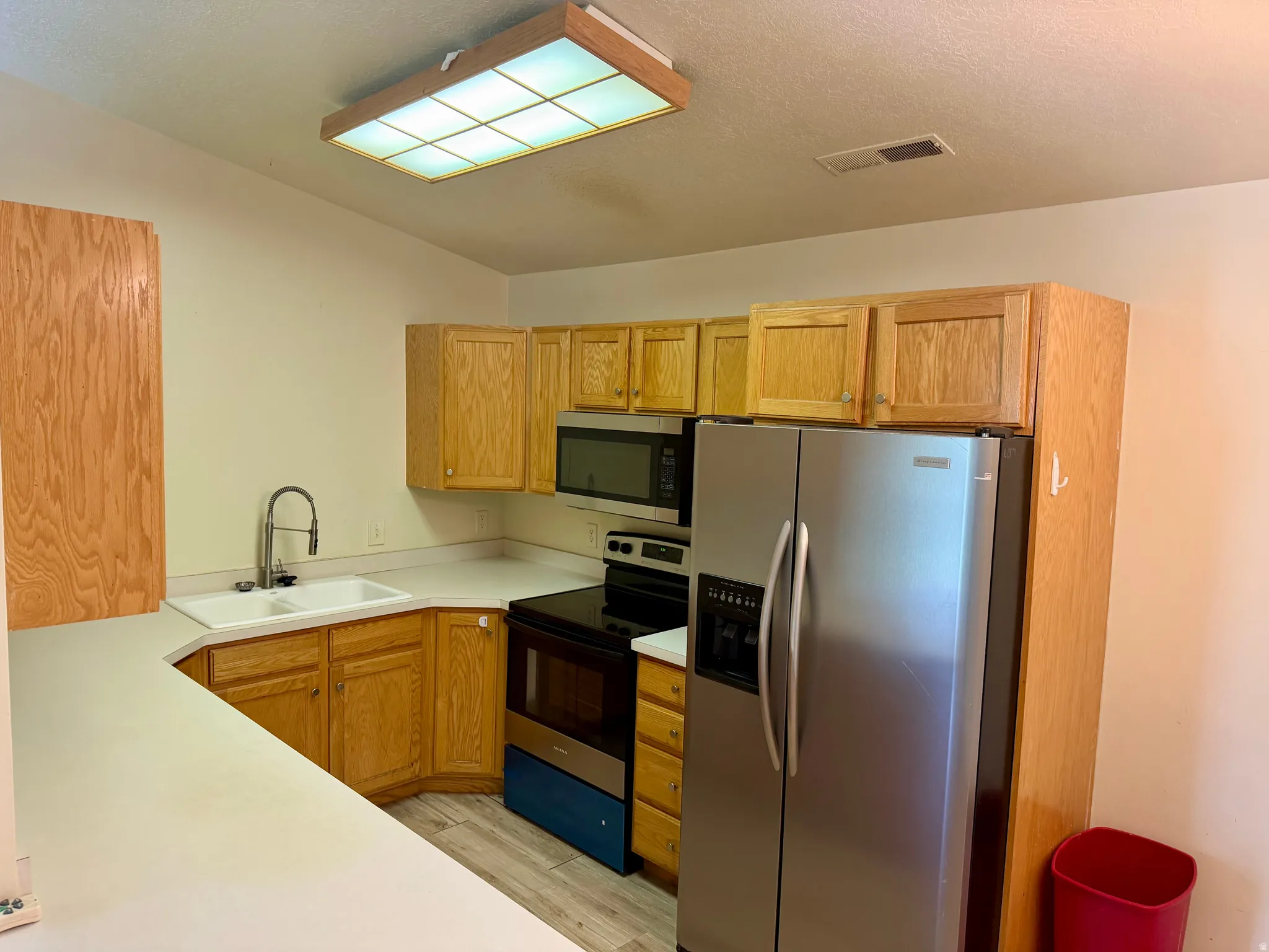 Kitchen featuring light wood cabinetry, stainless steel appliances, a double basin sink, and a multi-pane ceiling light fixture