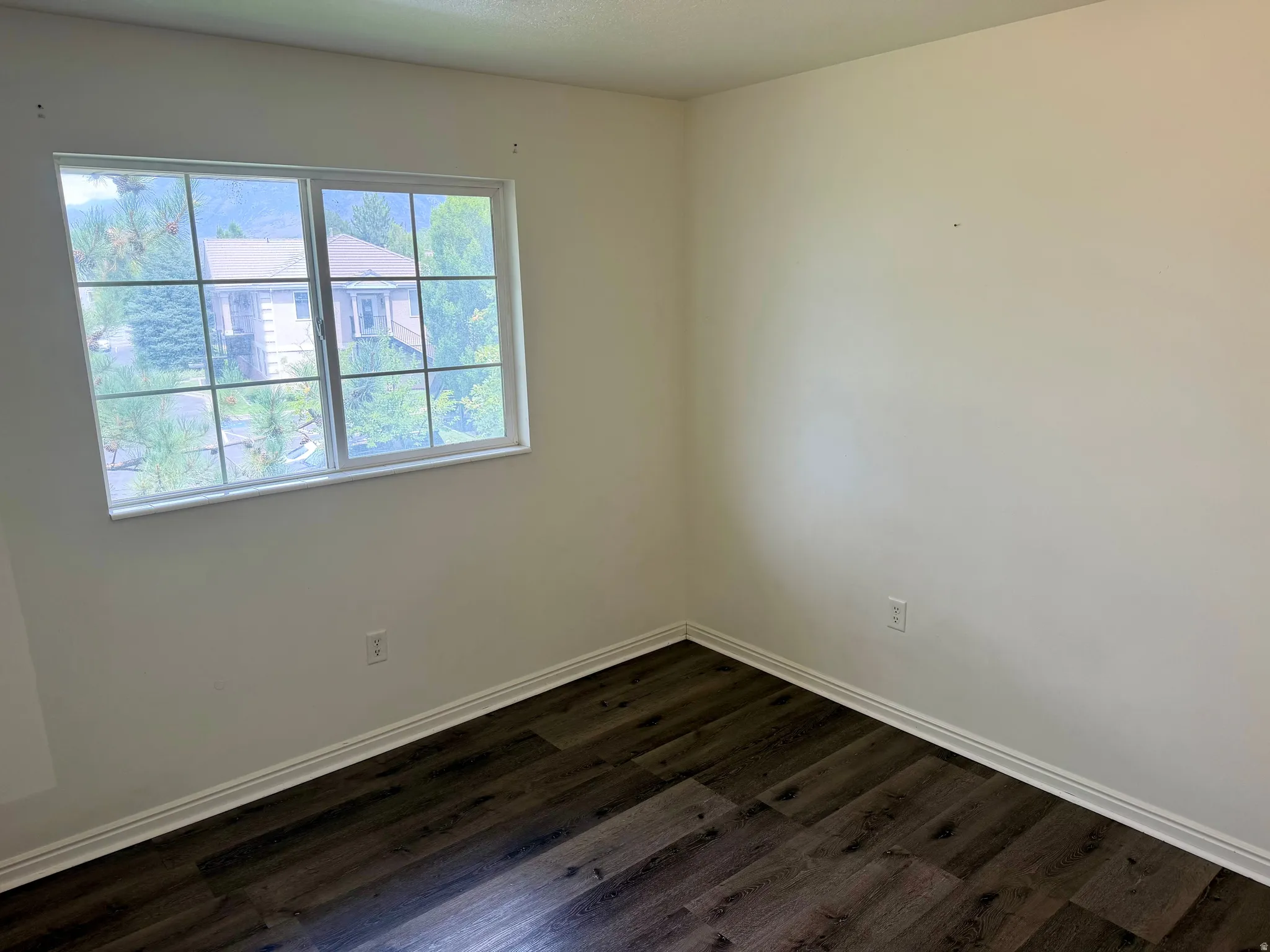 White walls with a single window, dark wood-finish flooring, and white trim molding