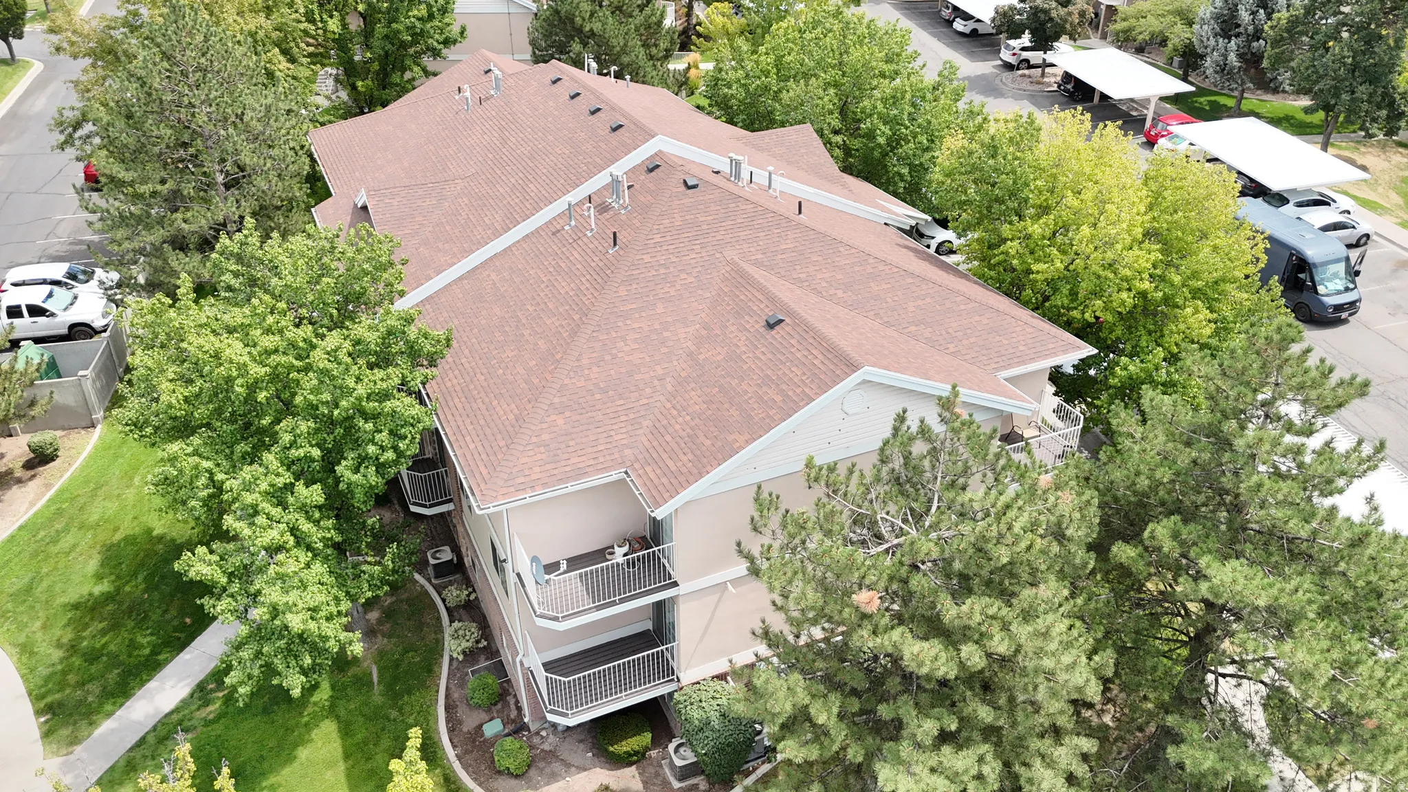 Multi-level building with a brown shingle roof, exterior balconies, and surrounding mature trees