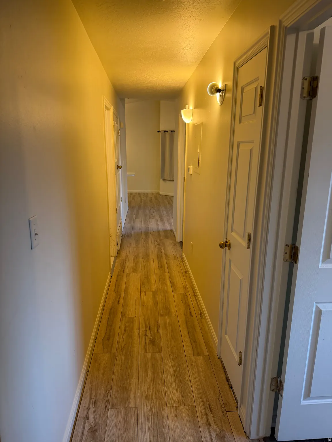 Hallway featuring wood-finish flooring, white paneled doors, and wall-mounted sconces