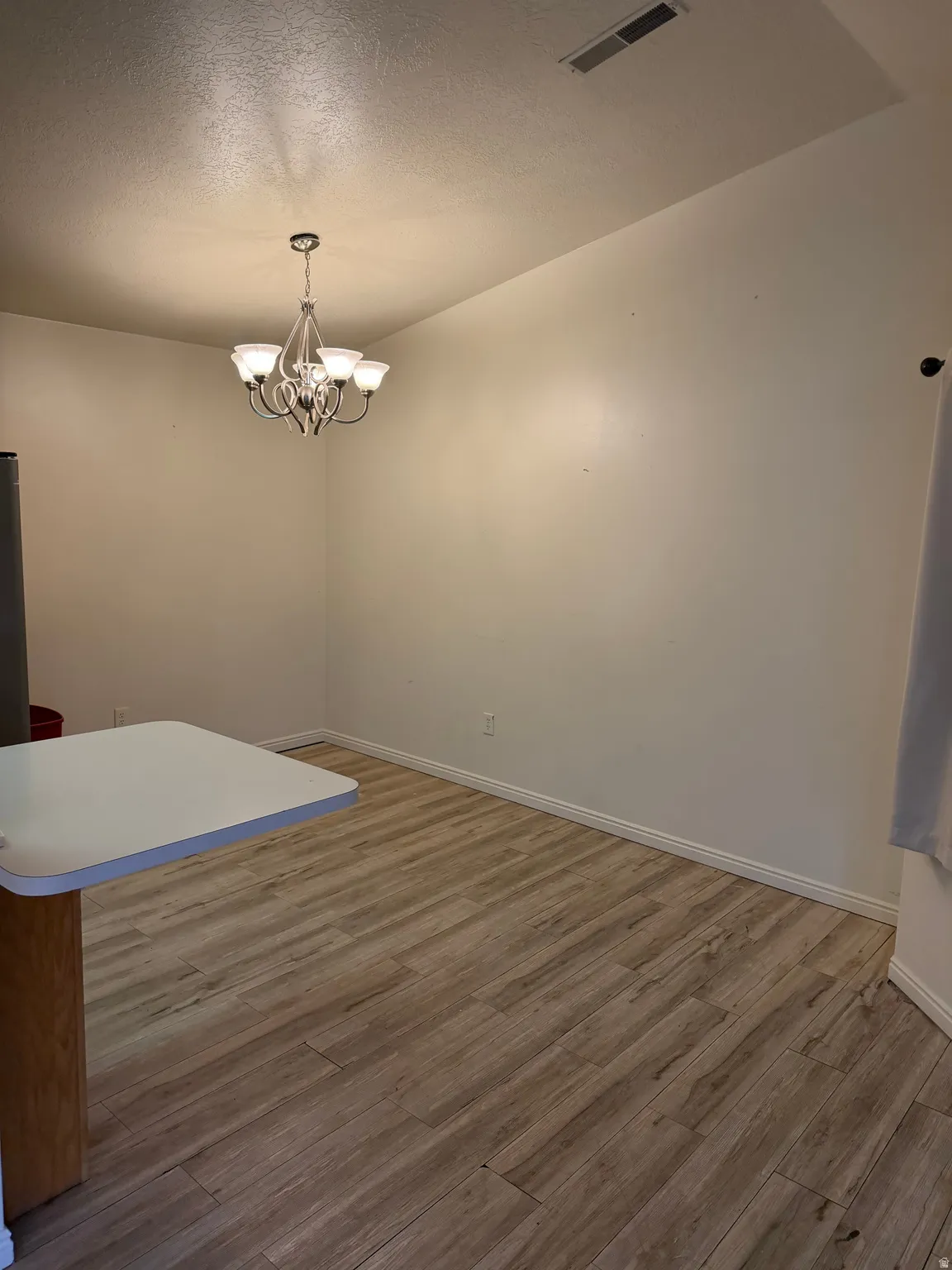 Wood-finish flooring, white baseboards, and a chandelier with glass shades