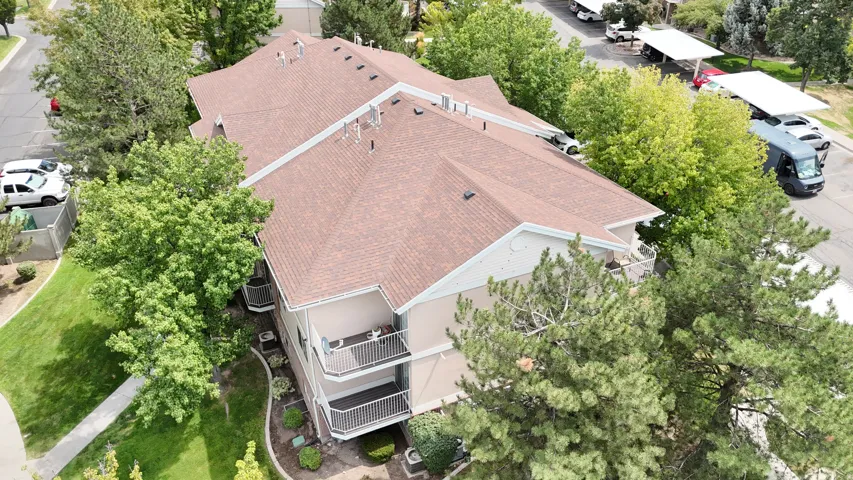 Multi-level building with a brown shingle roof, exterior balconies, and surrounding mature trees