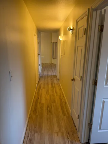 Hallway featuring wood-finish flooring, white paneled doors, and wall-mounted sconces