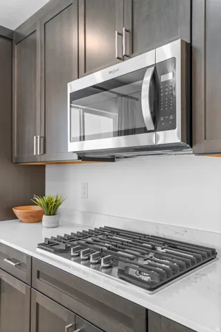 Stainless steel microwave, built-in cooktop with griddle, white quartz countertops, subway tile backsplash, and dark wood-finish cabinetry