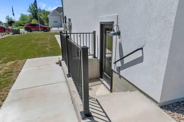 Concrete walkway leading to a private exterior entrance with a black metal railing and a wall-mounted light fixture