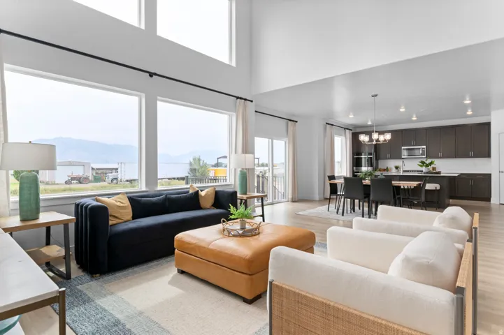 Expansive open-concept living area with high ceilings, large windows, wood-finish flooring, a contemporary kitchen with dark wood cabinetry, and a dining area with a modern chandelier