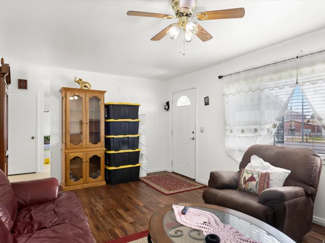 Wood-finish flooring throughout, white walls, and a ceiling fan with integrated lighting